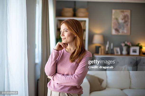 serene woman contemplating at home by the window - hand on chin stock pictures, royalty-free photos & images