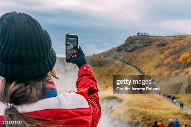 junge frau, die ein selfie am gullfoss-wasserfall in island macht - reiseroute golden circle stock-fotos und bilder