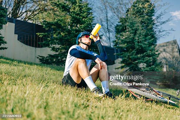 cyclist drinking from water bottle while resting on grassy hillside - cyklist bildbanksfoton och bilder