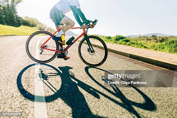 cyclist enjoying sunny day on cycle ride casting long shadow on asphalt - road cycling stock pictures, royalty-free photos & images
