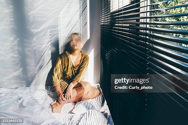 a sad, depressed woman sitting on the bed. long exposure photo. - disperazione foto e immagini stock