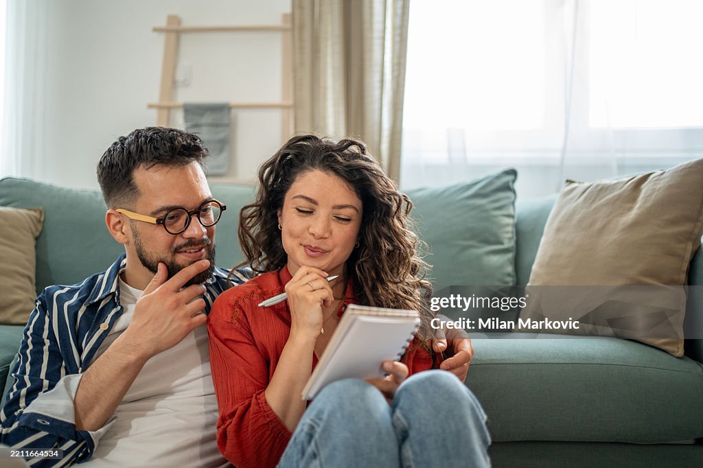 Young couple sitting on floor taking notes and planning finances
