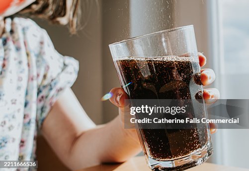 A child pours a red can of fizzy drink into a glass she is holding with her other hand A child pours a red can of fizzy drink into a glass she is holding with her other hand