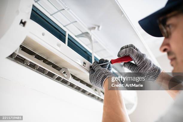 technician with screwdriver repairing air conditioner at home - airconditioning stockfoto's en -beelden