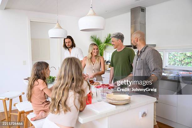 parents and friends smiling and making food in kitchen with two girls sitting at island - villa stock pictures, royalty-free photos & images