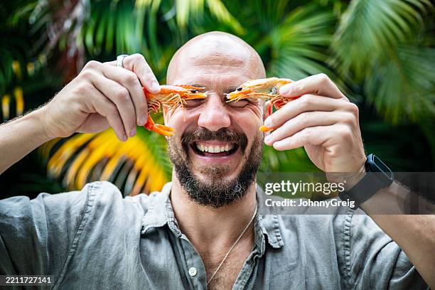 reifer mann mit bart, lächelnd und zwei garnelen vor den augen haltend - byron bay stock-fotos und bilder