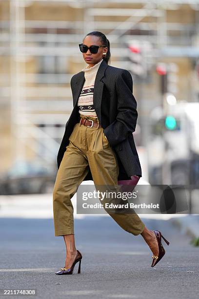 Emilie Joseph wears a black pinstripe oversized blazer over a cream turtleneck sweater featuring a geometric multicolor pattern, tucked into...