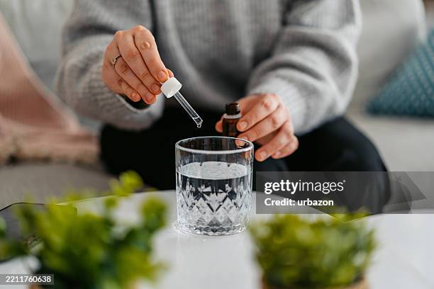 mujer joven poniendo gotas de medicina en un vaso de agua - cuentagotas fotografías e imágenes de stock