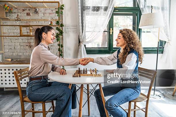 zwei junge frauen schütteln sich die hände, nachdem sie schach gespielt haben - fairness stock-fotos und bilder