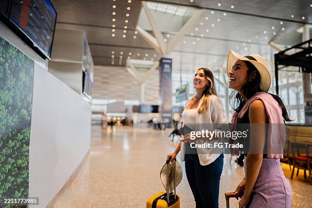 young friends checking the arrival departure panel at the airport - mala de rodinhas imagens e fotografias de stock