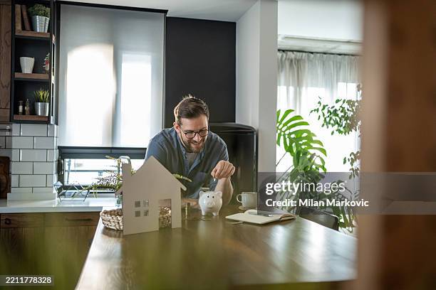 young man saving money for new house in piggy bank - welvaart stockfoto's en -beelden