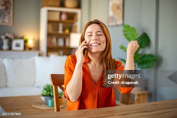 happy woman receiving good news on the phone at home - tears of joy stock pictures, royalty-free photos & images