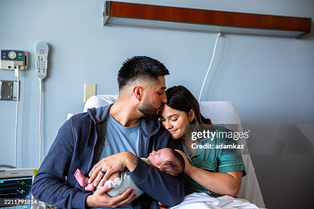 junge eltern, die ihren neugeborenen jungen im krankenhausbett halten - neu stock-fotos und bilder
