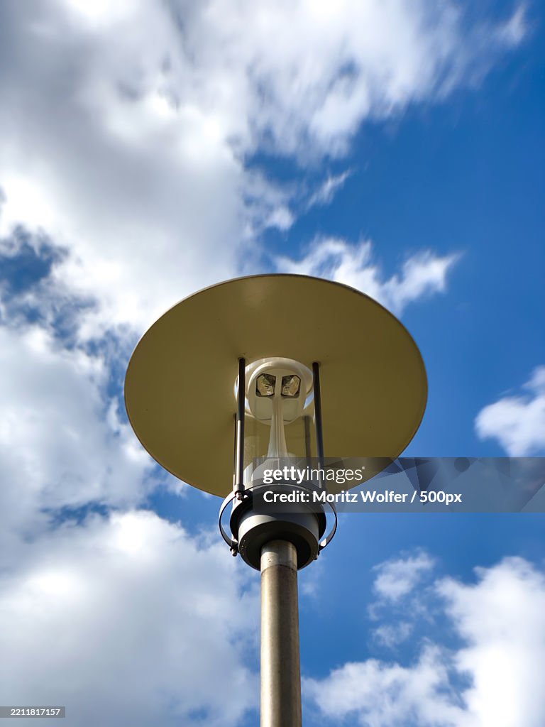 Low angle view of a street light pole against sky with clouds