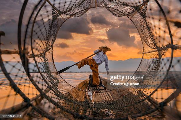 burmesischer fischer balanciert auf boot und hält fischernetz bei sonnenuntergang im inle-see - südostasien stock-fotos und bilder