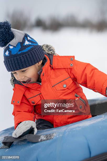 young child enjoying snow tubing in a bright orange winter jacket - family day trips stock pictures, royalty-free photos & images