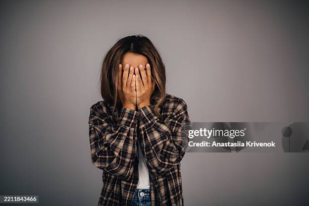 young woman covering face in plaid shirt against neutral background - hands covering eyes stock pictures, royalty-free photos & images