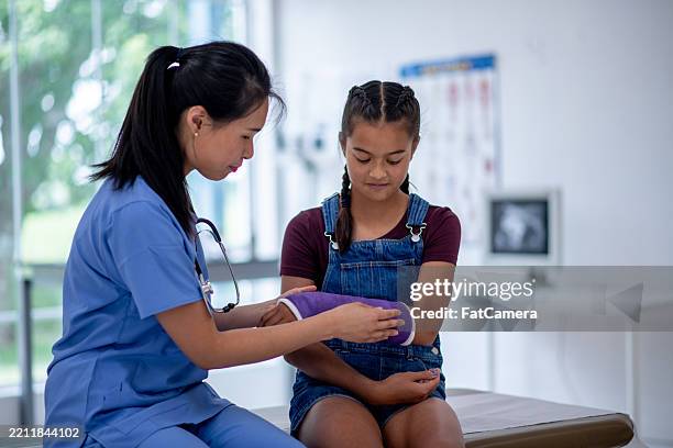 weibliche ärztin, die mädchen mit armgips im medizinischen untersuchungsraum assistiert - armbruch stock-fotos und bilder