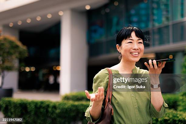 smiling businesswoman talking on speakerphone outdoors in urban environment - conference phone stock pictures, royalty-free photos & images
