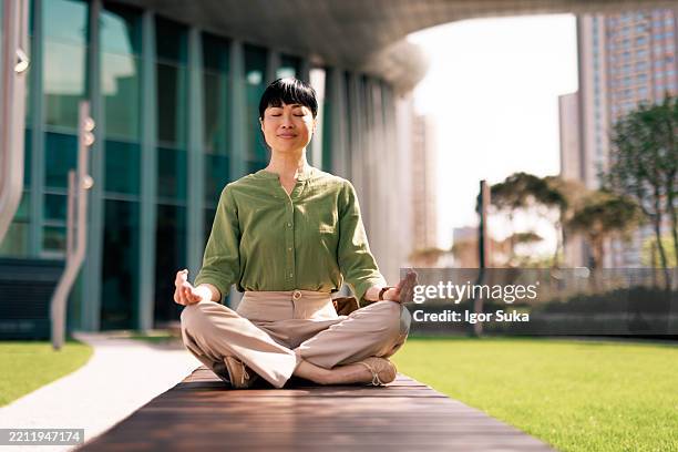 businesswoman meditating outdoors in the lotus position - lotus position stock pictures, royalty-free photos & images