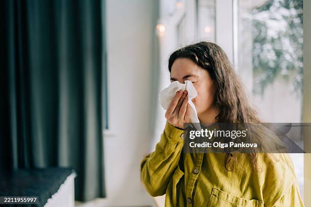 sick woman blowing her nose with tissue paper at home, suffering from allergy or flu - human nose stock pictures, royalty-free photos & images