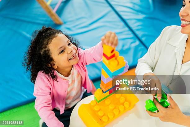 child girl and teacher playing with toy blocks at playroom - ergotherapie stockfoto's en -beelden