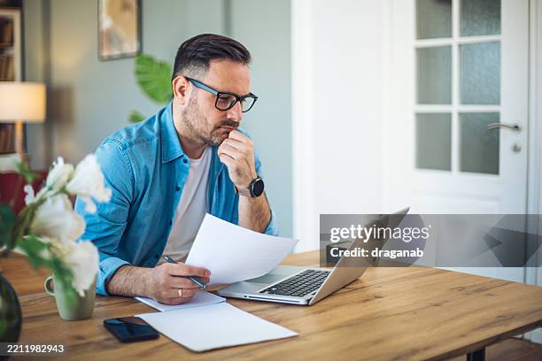 man working from home office analyzing documents and using laptop - checking documents stock pictures, royalty-free photos & images