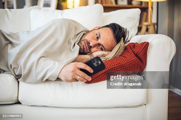 bored man lying on sofa using smartphone at home - social isolation stock pictures, royalty-free photos & images