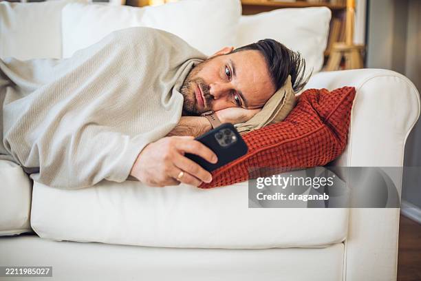 bored man lying on sofa using smartphone at home - ligga ner bildbanksfoton och bilder