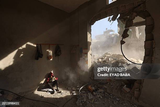 Palestinian boy holds a book as he sits in rubble of a house, following overnight Israeli strikes, at the Nuseirat refugee camp in the central Gaza...