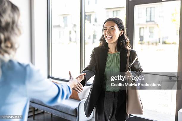 businesswomen shaking hands in modern office lobby - new hire stock pictures, royalty-free photos & images