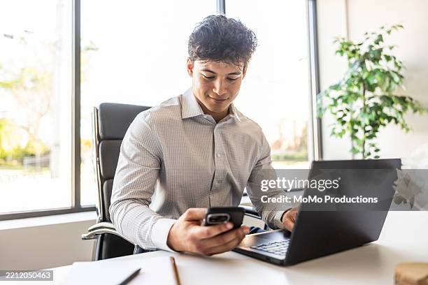young businessman using smartphone and laptop in modern conference room - multi tasking stock pictures, royalty-free photos & images