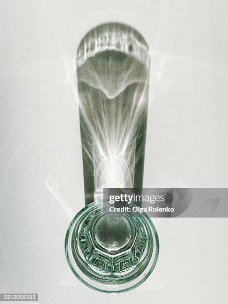 glass of water casting an elongated shadow on white background - stillleben stock-fotos und bilder
