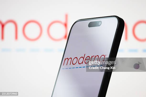 In this photo illustration, the logo of Moderna, Inc. Is displayed on a smartphone screen, with the company's branding visible in the background, on...