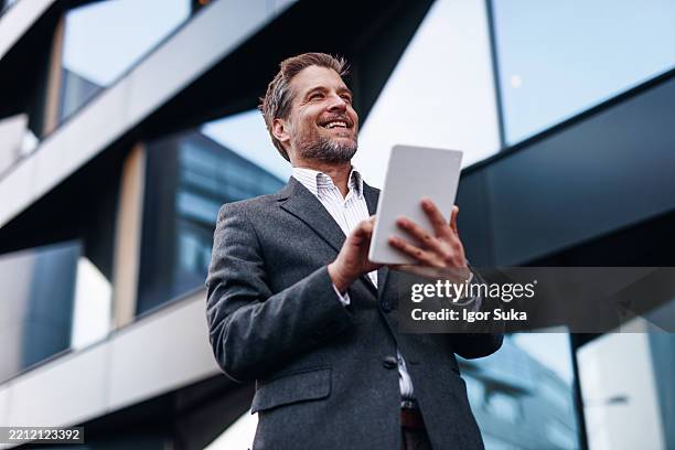 smiling businessman using digital tablet in front of modern office building - executivo de vendas imagens e fotografias de stock