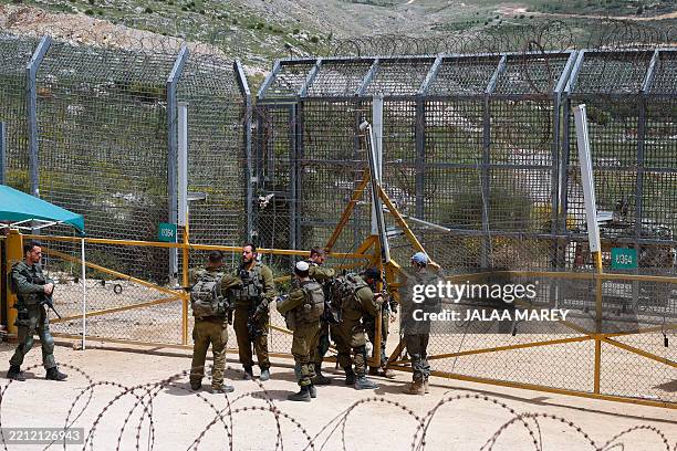Israeli soldiers stand guard as Druze men demonstrate in solidarity with the Syrian Druze community near the border barrier in the village of Majdal...