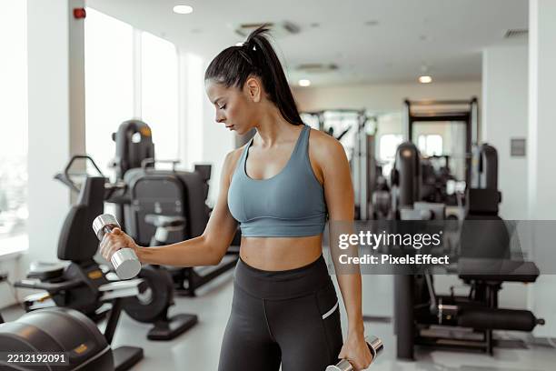 femme athlétique montrant sa force avec des haltères à la salle de sport - body building photos et images de collection