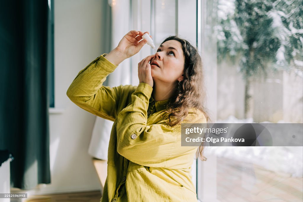 Woman using eye drops at home during winter season