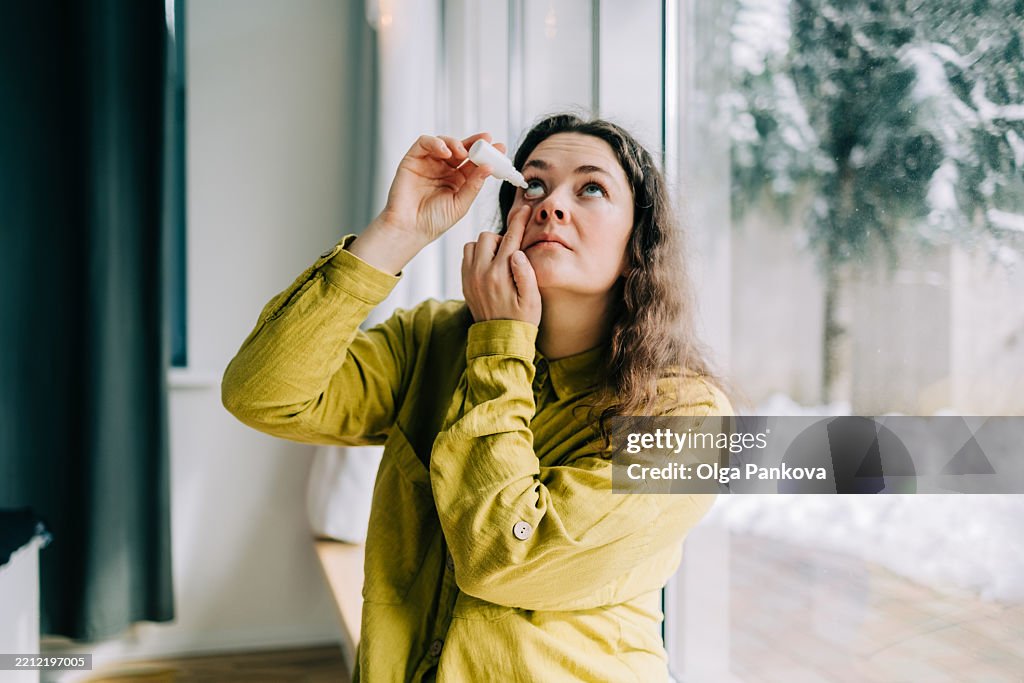 Woman using eye drops at home during winter season