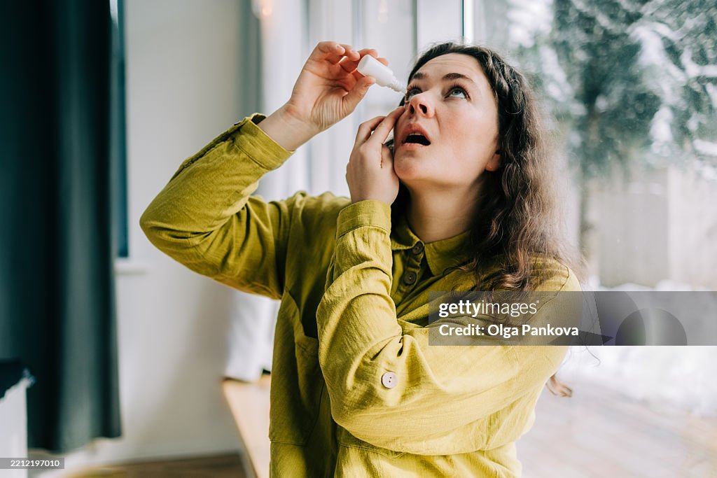 Woman using eye drops at home during winter season