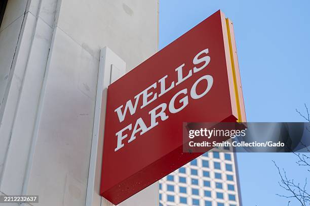 Wells Fargo sign mounted on building exterior with skyscraper in background, Financial District, San Francisco, California, March 18, 2025.