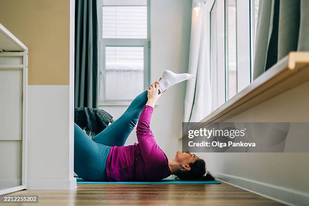 mid adult woman practicing yoga at home holding her leg and stretching - leggings stock pictures, royalty-free photos & images