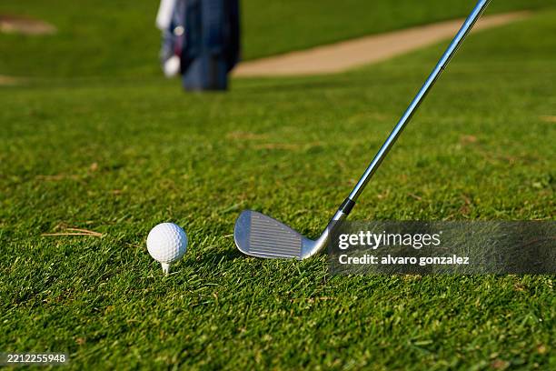 golfer aiming golf ball on tee with club on lush green course - golf club stock pictures, royalty-free photos & images