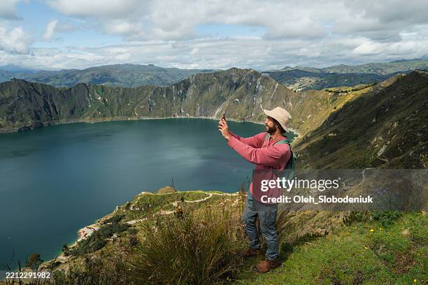 man photographing with smartphone hiking around quilotoa lake crater in ecuador - hi tec adventure racing series stock pictures, royalty-free photos & images