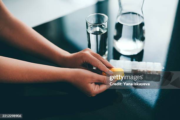hands holding supplement with glass of water and weekly pill organizer on desk - hormone therapy stock pictures, royalty-free photos & images