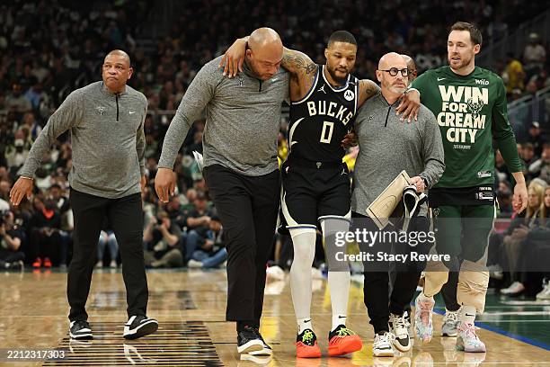 Damian Lillard of the Milwaukee Bucks is helped off the court after an apparent injury during the first quarter in Game Four of the Eastern...