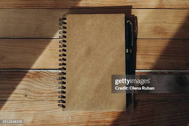 closed spiral notepad with a pen lying in sunlight on wood planks. - closed book on table stock pictures, royalty-free photos & images
