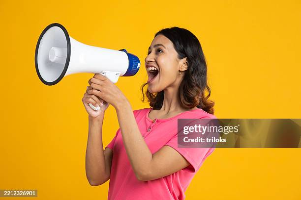 woman shouting over megaphone on yellow background - megafone imagens e fotografias de stock
