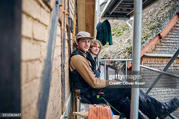portrait of two carpenters sitting on scaffolding at a house under construction - fachwerk stock-fotos und bilder