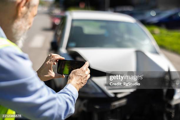 man taking photos of his wrecked car for insurance purposes after a crash - acidente de carro imagens e fotografias de stock